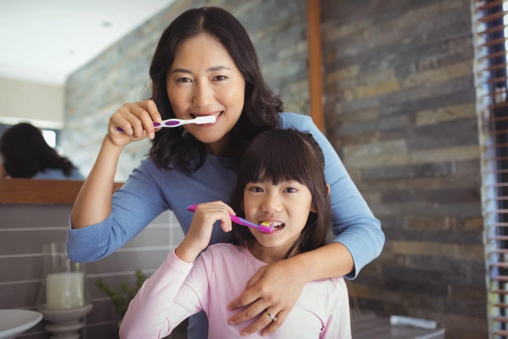 Portrait of mother and daughter brushing teeth in the bathroom